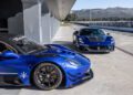 Two blue Maserati cars, including a sleek GT2 Stradale, grace the garage area. One is parked sideways showcasing its side and rear, while the other faces forward. A stunning mountain backdrop evokes the picturesque charm of Spain.