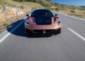 A bronze Maserati sports car with a black hood races along a rural road, framed by the rocky hills and lush greenery of Spain.