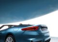 The Maserati GranCabrio, a blue convertible sports car with striking red taillights, sits partially visible under a large, curved metallic structure.