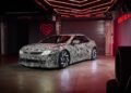 A camouflaged car with swirling patterns, possibly hinting at the BMW Vision, is parked indoors, illuminated by red neon lighting and surrounded by various automotive elements.