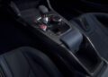 Close-up of a BMW M4 CS's central console, showcasing a gear shifter, control knobs, and a start button, all enveloped in sleek carbon fiber and luxurious leather seats.