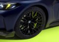 Close-up of a dark blue BMW M4 CS's front wheel, showcasing intricate black alloy rims and its signature logo, set against a neon green background—perhaps a nod to Valentino Rossi's vibrant style on his 46th birthday.