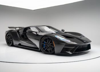 A sleek black Ford GT sports car with a low, aerodynamic design, large wheels, and a rear spoiler is parked in a white studio setting. The Liquid Carbon Edition subtly flaunts ghosted stripes that add an extra layer of intrigue to its flawless finish.