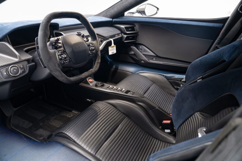 The interior of the Ford GT Liquid Carbon Edition boasts black leather seats accented with ghosted stripes, a sporty steering wheel, and a sleek dashboard featuring various control buttons and displays.