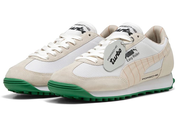A pair of white and beige automotive-inspired PUMA sneakers with green soles, Porsche Turbo branding, mesh panels, and a tag attached to the laces—perfect for any driver seeking style and performance.