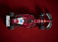 Top view of a sleek SF-25 F1 car, adorned with prominent sponsor logos, set against a striking dark red background.