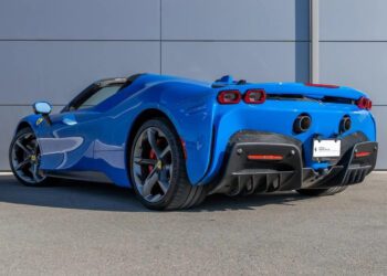 A sleek blue SF90 Spider is parked in front of a gray wall, its elegant form captured from the rear left side.