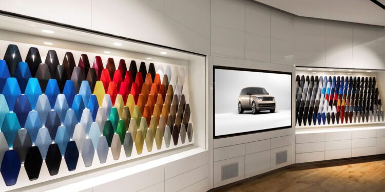 The showroom wall showcases an array of vibrant car paint samples, highlighted by a screen featuring an SUV image. Jaguar Land Rover invests $81.2M to expand paint facilities, reflecting their commitment to innovation and quality in every hue.