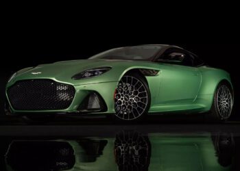 A green sports car with a sleek design and distinctive alloy wheels, reminiscent of expensive Aston Martins, is set against a black reflective surface.