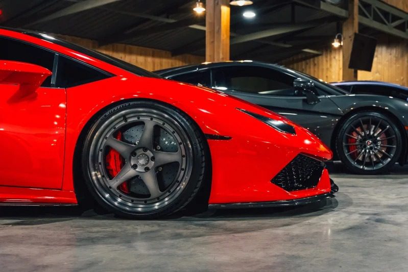 Close up a red exotic car and a black sports car that is parked inside and highlights its front ends and bikes and shows the attraction of hypercars.