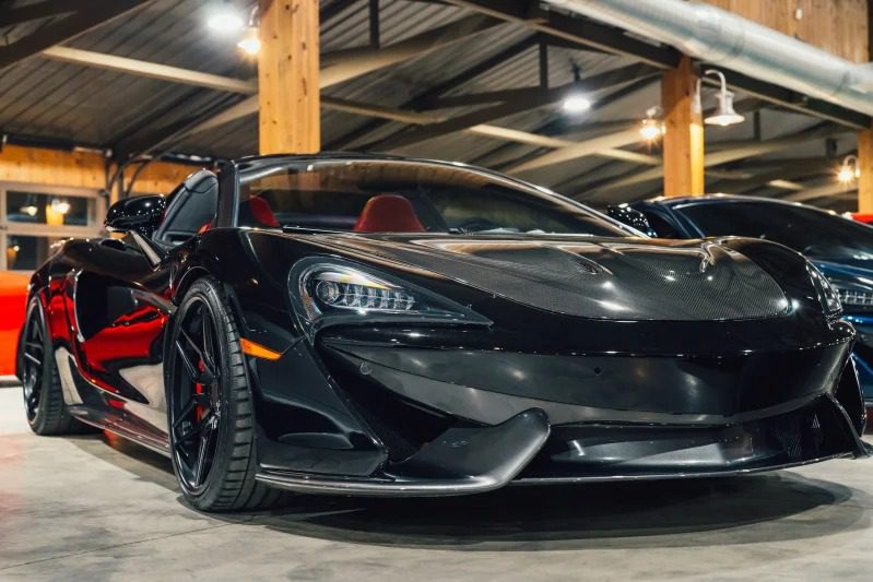 An elegant black hypercar with a red interior, which is parked in industrial lighting inside, radiates a hint of exotic auto-aura.