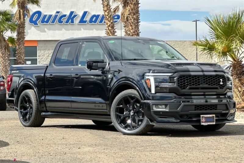 A black four-door Ford F-150 truck is parked outdoors on a sunny day near palm trees and a building with a "Quick Lane" sign, showcasing this impressive vehicle that’s now for sale.