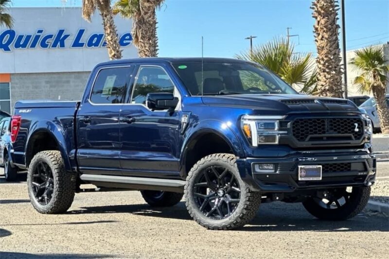 A dark blue Ford F-150 pickup truck is parked outdoors on a sunny day near palm trees and a building with a "Quick Lane" sign, and is now For Sale.