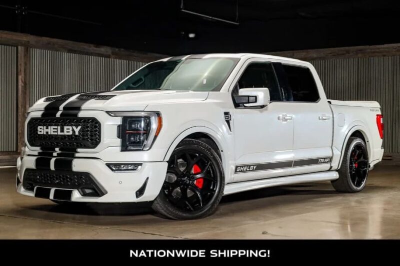 A white Shelby Ford F-150 with black racing stripes and red brake calipers is parked indoors—an impressive option for those seeking Shelby Trucks or Ford F-150 trucks for sale.
