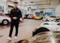 A person stands in a garage lined with various sports cars, including a white Porsche Formula E in the foreground. The bright overhead lighting and tiled floor evoke the sleek luxury of Miami.