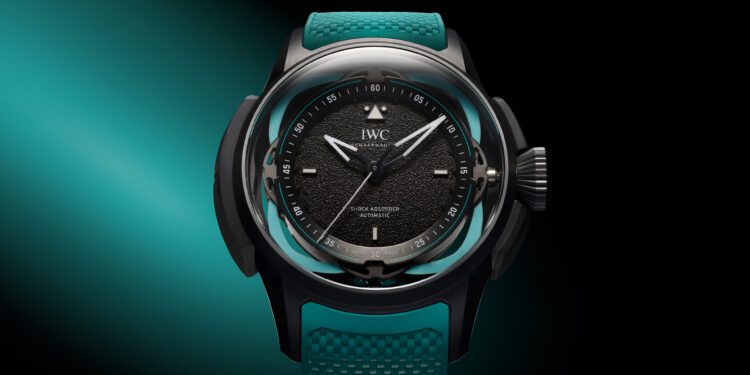 A black watch with a textured dial, luminescent hands, and teal accents is elegantly showcased against a gradient aqua and black background, inspired by the Toto Wolff Edition Big Pilot’s Watch.