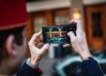 A person in a red hat captures a stunning photo of a parked Rimac sports car with their smartphone, focusing on the sleek vehicle in front of the I.C.E. St. Moritz entrance.