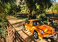 The RUF Rodeo, an orange classic sports car, is parked on a dirt road surrounded by trees and fencing, basking in bright sunlight—a truly unique display.