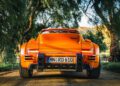 Amidst a forested backdrop, the vibrant orange sports car proudly boasts a "Rodeo" badge, hinting at its connection to the exclusive RUF Rodeo. Its German "MN RD 610" plate gleams under the sun on this picturesque dirt road.