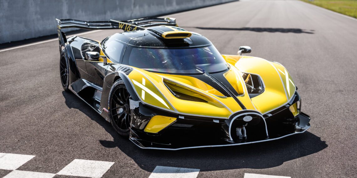 A sleek yellow and black Bugatti Bolide hypercar is parked on a racetrack near distinctive checkered markings, ready for its shakedown test.