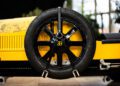 A black wheel with a Bugatti logo graces the side of a yellow vehicle, reminiscent of the craftsmanship at Hedley Studios, secured by two leather straps.