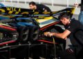 A mechanic works on the exhaust of a Bugatti W16 Mistral, with another hypercar in the background undergoing a shakedown test on the racetrack.