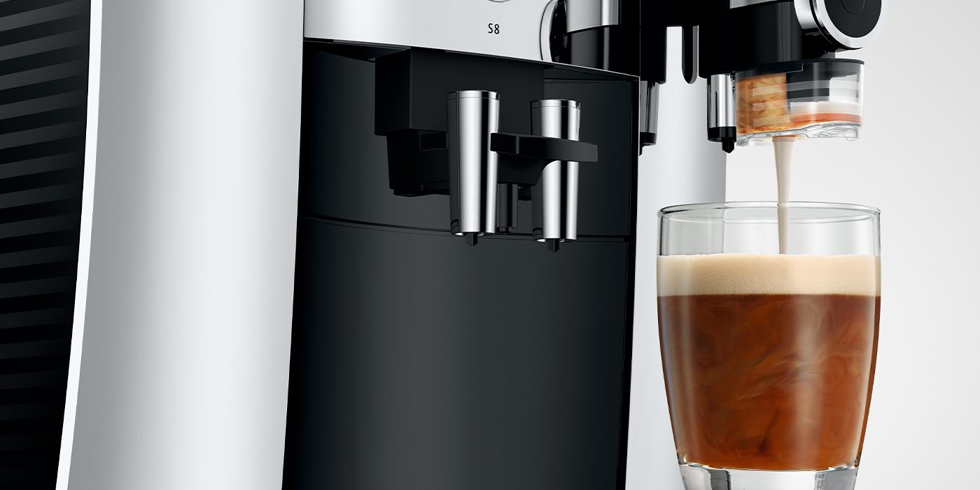 The JURA S8 coffee machine elegantly dispenses frothy coffee into a glass, showcasing its modern design with sleek black and silver elements. It's the epitome of coffee enjoyment, blending innovation with style for the perfect brew every time.