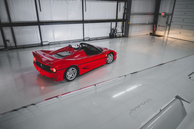 A pristine Ferrari F50 is parked in a spacious, well-lit garage with white flooring and large doors, ready for its moment at the RM Sotheby's auction, where it's anticipated to fetch a world record price.