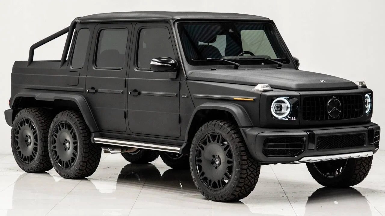 A matte black Mercedes-Benz six-wheeled SUV, inspired by 6x6 trucks, with rugged tires is parked indoors on a white floor.