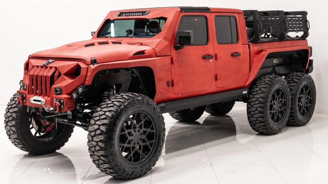 A custom red 6x6 truck with large off-road tires, black grille, and a cargo rack, photographed indoors on a white background—perfect for those seeking unique 6x6 trucks for sale.