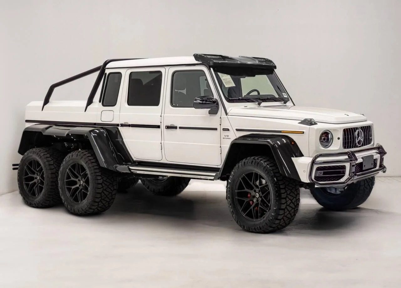 A white six-wheeled Mercedes-Benz G-Class pickup truck, a stunning example among 6x6 trucks for sale, is parked in a well-lit indoor studio with a plain background.