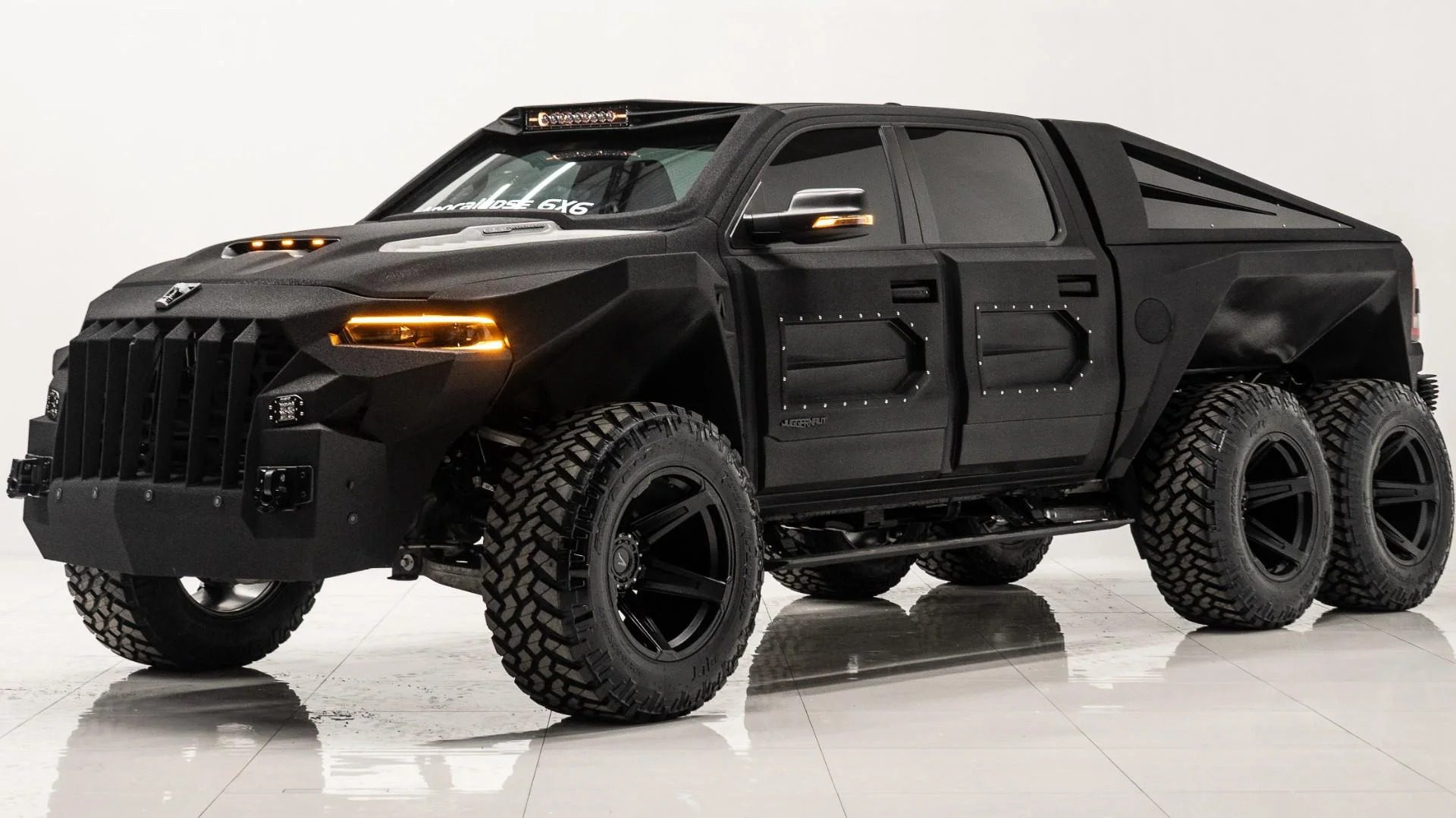 A large, matte black 6x6 truck with rugged off-road tires, sharp angles, and tinted windows is parked on a glossy white floor—an impressive pick among 6x6 trucks for sale.