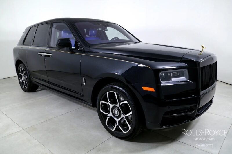 A black Rolls-Royce Cullinan luxury SUV is parked indoors on a light-colored floor, viewed from the front left side with the hood ornament visible.