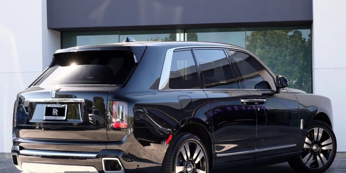 A black Rolls-Royce Cullinan luxury SUV is parked outside a modern building on a sunny day.