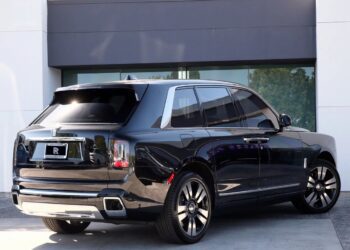 A black Rolls-Royce Cullinan luxury SUV is parked outside a modern building on a sunny day.