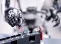 In a workshop setting, a robotic hand deftly manipulates a piece of metal near a mechanical assembly, showcasing the finesse of AI technology.