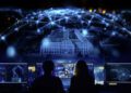 Two people sit in front of computer screens displaying AI and data on humanoid robots, while a digital network and a building with lit windows loom in the background, evoking the precision and innovation akin to Mercedes-Benz.