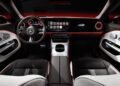 A modern Mercedes-Benz car interior with an illuminated dashboard and digital display, complemented by black and white seating with red accents. The steering wheel proudly features the iconic Mercedes logo, while the innovative AI Radio App adds a touch of future-ready tech inspired by will.i.am.