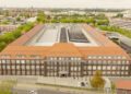 Aerial view of a Mercedes-Benz facility, its U-shaped building flaunting a red roof, surrounded by trees and cityscape.