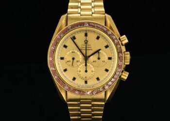 The dazzling 18k Gold Omega Speedmaster watch, reminiscent of the timepiece Neil Armstrong wore, boasts a tachymeter scale on a striking red bezel, three sub-dials, and a link bracelet. Its elegance is perfectly captured against a deep black background.
