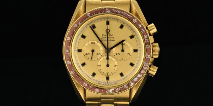 The dazzling 18k Gold Omega Speedmaster watch, reminiscent of the timepiece Neil Armstrong wore, boasts a tachymeter scale on a striking red bezel, three sub-dials, and a link bracelet. Its elegance is perfectly captured against a deep black background.