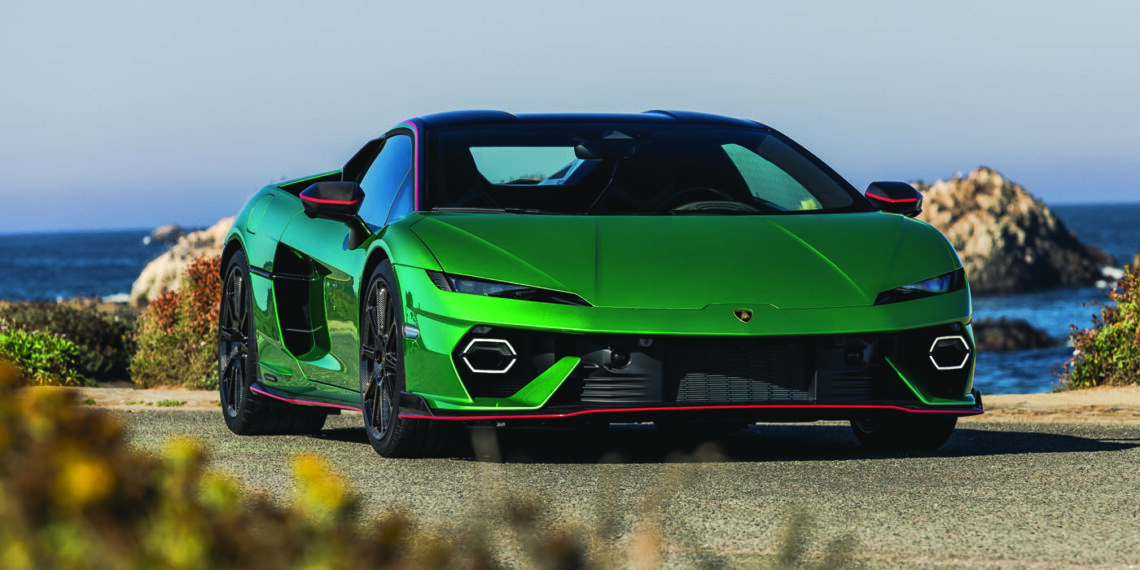 A sleek Lamborghini sports car, known as the Charging Bull, is parked on a coastal road with stunning ocean views and rugged rocks in the background.