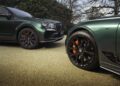 Two green luxury cars from the Le Mans Collection rest on a gravel surface. Their black alloy wheels with orange brake calipers proudly display the "B" logo, hinting at their Bentley heritage. Trees and shrubs provide a lush backdrop for this stunning Bentayga Apex duo.