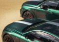 Two green luxury cars from the Le Mans Collection, including a Bentley Bentayga Apex, are elegantly parked on a sunlit pavement, captured from an elevated angle.