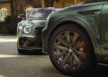 A close-up of two green luxury Bentleys parked, featuring a focus on a front wheel adorned with a prominent "B" logo in the foreground and part of another car gracefully showcased in the background.