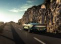 A sleek Aston Martin Vanquish speeds up a winding mountain road with rocky cliffs on either side, under a clear sky.