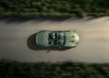 Overhead view of an Aston Martin Vanquish, a green convertible sports car, cruising along the road. Surrounded by blurred greenery and with a person inside, this sleek vehicle showcases the elegance of one of the fastest front-engined convertibles.