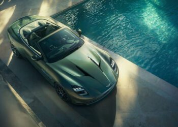 A sleek Aston Martin Vanquish, the fastest front-engined convertible, sits elegantly beside a pool, with the sun casting enticing shadows over its luxurious curves.