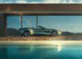 An Aston Martin Vanquish convertible is parked before a modern glass-walled building, its sleek front-engine design reflected in the swimming pool. In the distance, a breathtaking mountainous landscape looms, echoing the allure of one of the fastest convertibles on the road.