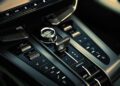 Close-up of a car center console in an Aston Martin Vanquish, featuring a gear selector knob, buttons for temperature control, fan speed, drive modes, and manual shifting. Its sleek and modern design complements the world's fastest convertible experience.